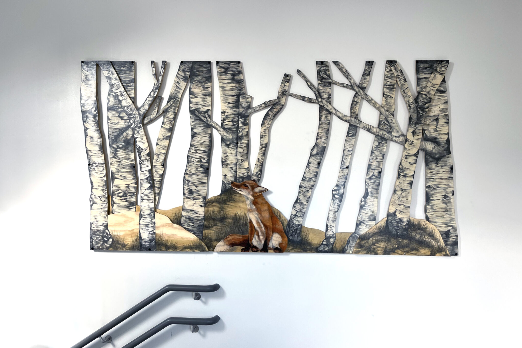 En bild av en teckning på figursågad plywood, föreställande en björkskog med en sittande räv